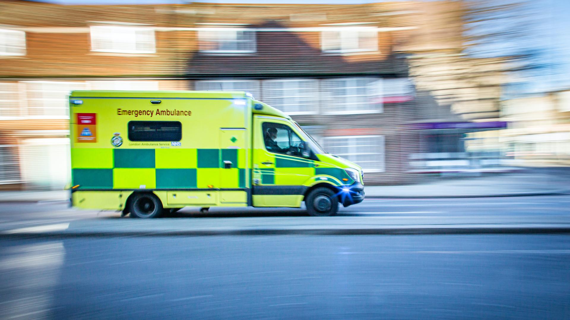 Ambulance driving quickly along a road, blurred houses in the background